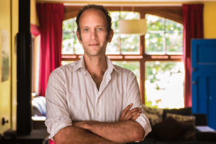 A man standing with his arms crossed and a window in the background.